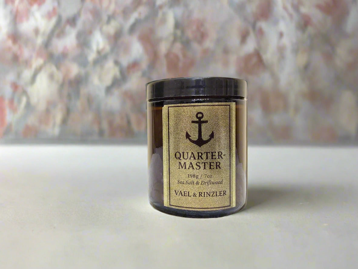 Jar of 'Quarter Master' candle by Vael & Rinzler on a textured surface with a beige background